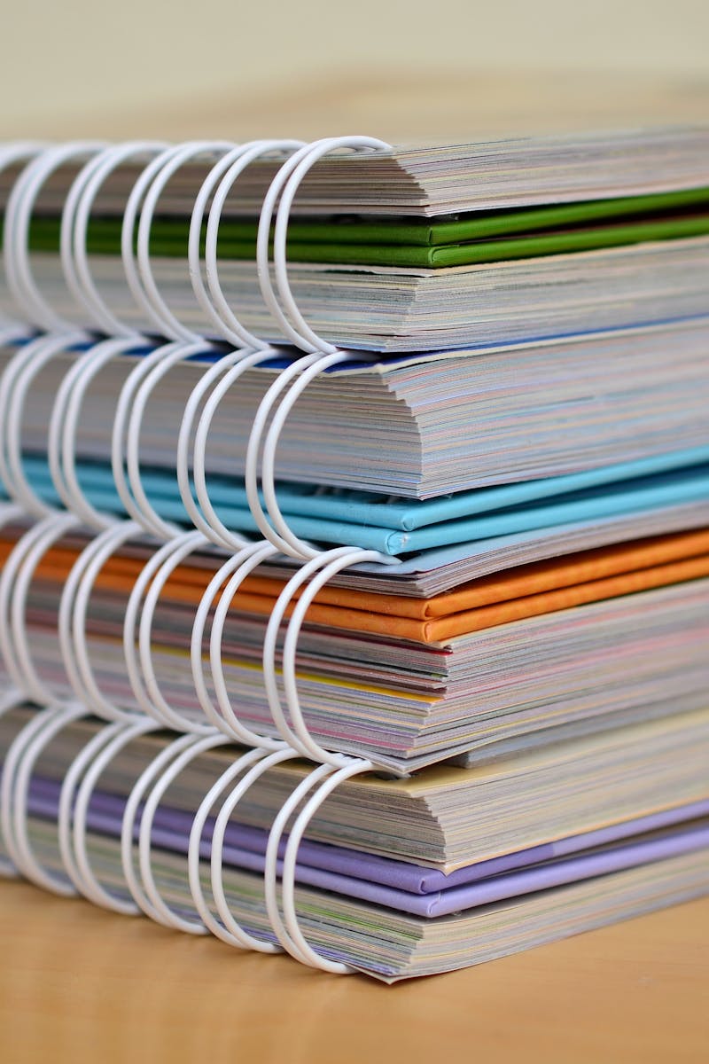 A colorful stack of spiral-bound notebooks neatly placed on a wooden desk. Ideal for educational themes.